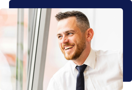 A smiling businessman in a white shirt and tie looking out a clean, bright office window